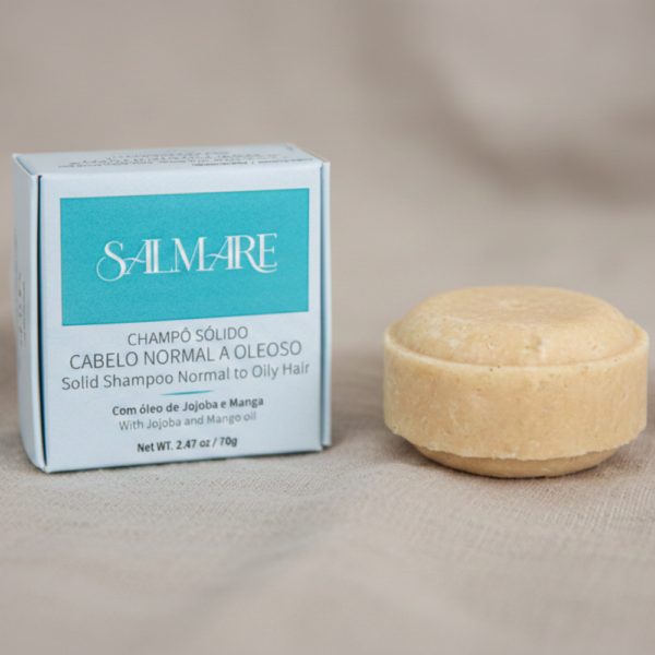 Champô Sólido Salmare para cabelos normais a oleosos. Barra redonda fora da caixa branca com rótulo azul texturado, pousada sobre tecido de linho bege natural. Contém Argila Verde e Óleo de Jojoba.
