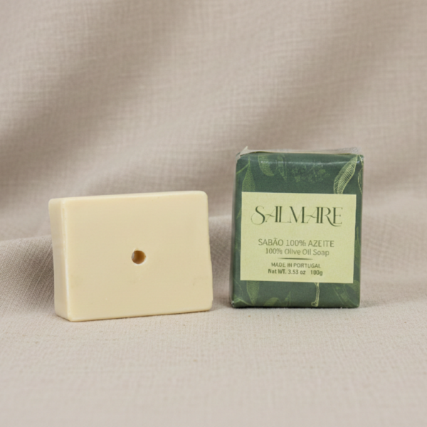 Sabão de Azeite Salmare barra redonda cor creme fora da embalagem branca com rótulo verde, pousado sobre tecido de linho bege natural. Produto artesanal com Azeite Virgem Extra.